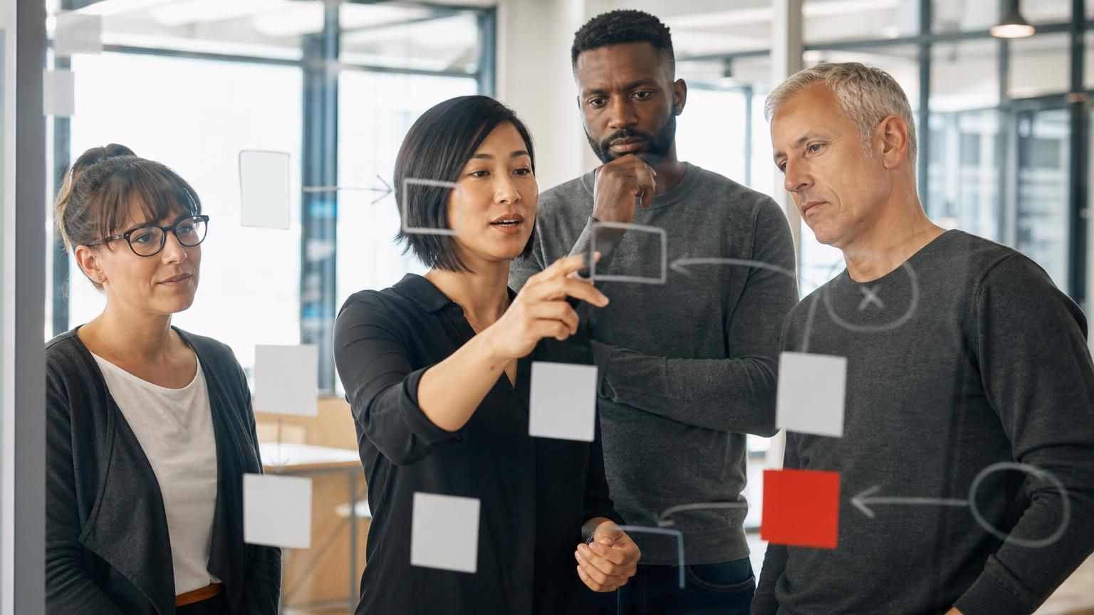 A team mapping out a process on a glass wall with sticky notes.